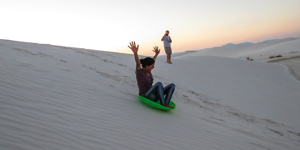 Woman riding a round sled down a sand dune at White Sands National Park in New Mexico