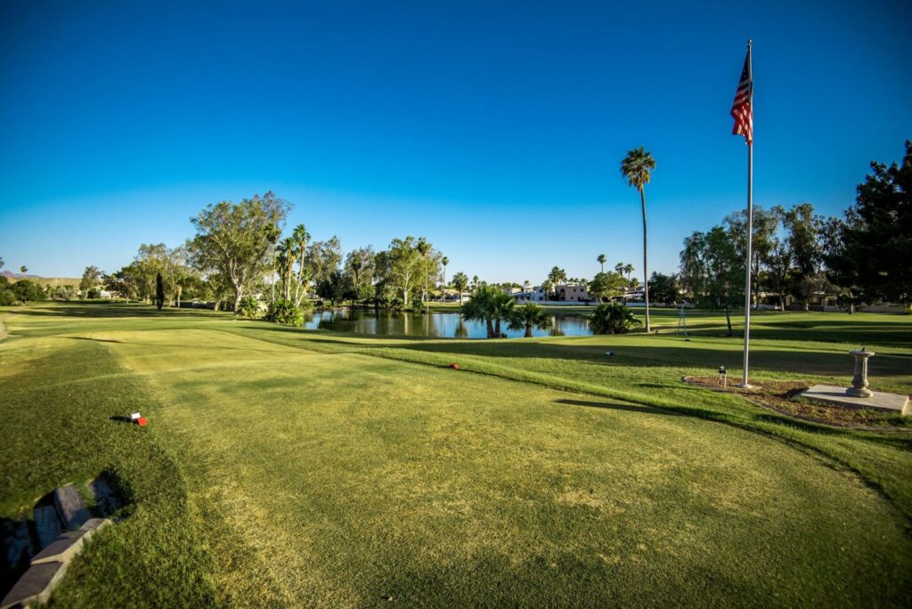 Lush, green, pristine golf course view. The sky is vibrant blue and there is an American flag blowing in the breeze.